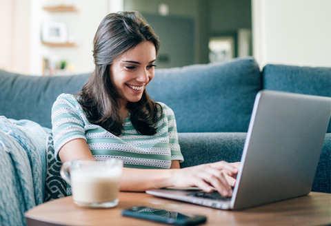 woman sitting against couch smiling at laptop